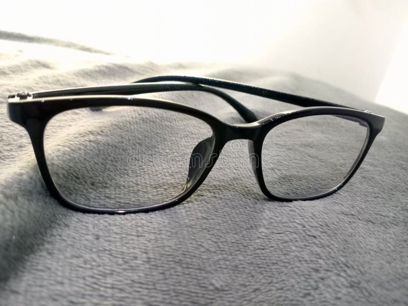 Black Eyeglasses Resting on Soft Grey Fabric. Simple rectangular eyeglasses with black frame on smooth surface