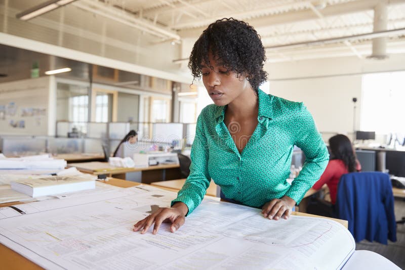 Black female architect studying plans in open plan office royalty free stock photo