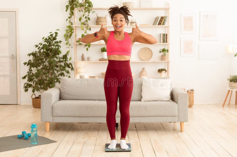 Black Fitness-flicka som ger tummenUpp på skalan hemma royaltyfri fotografi