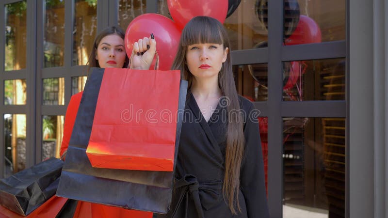 Black Friday stående av den allvarliga flickan som mycket visar av pappers- påsar med köp för flickvän med ballonger på mörker