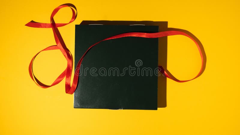 Black gift box tied with a red ribbon on the yellow background. Flat lay. Happy birthday concept. Present in a festive package stock image