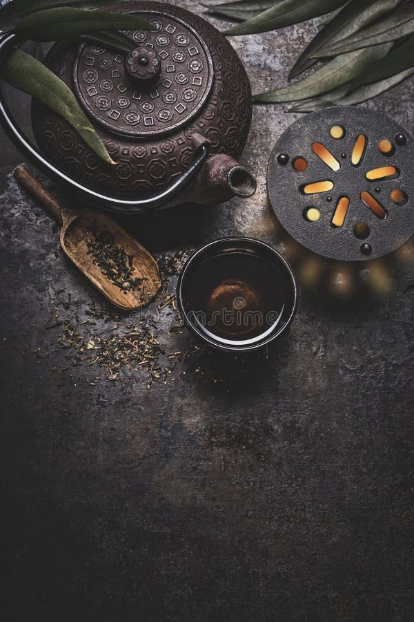 Black iron asian tea set on dark rustic background with teapot and fresh tea leaves, top view