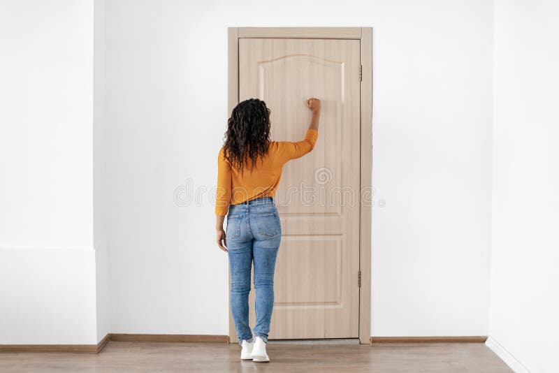 Black Lady Knocking At Entry Door Of Apartment, Back View