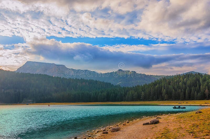 Black lake in Durmitor national park in Montenegro, Europe. Mountain, forest and beach on blue cloudy sky a sunny day at sunset.