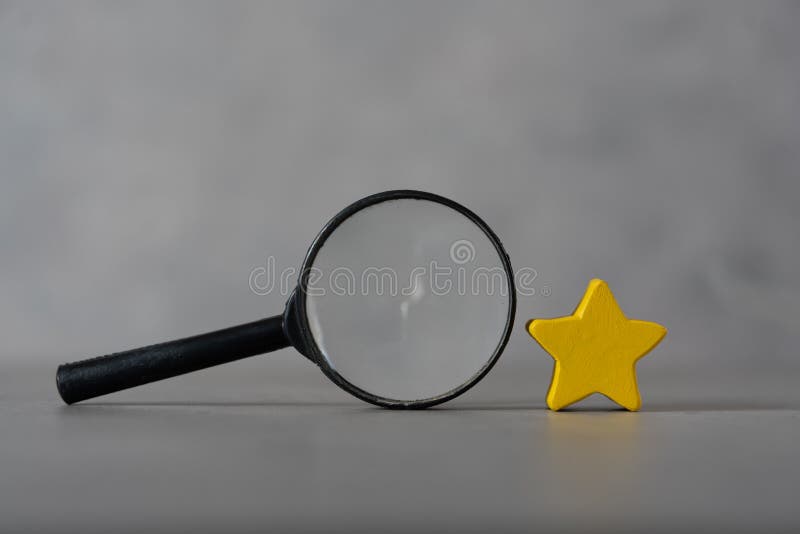 A black magnifying glass with a yellow star. The concept of finding the star, find a new actor. Hiring and recruitment selection royalty free stock image