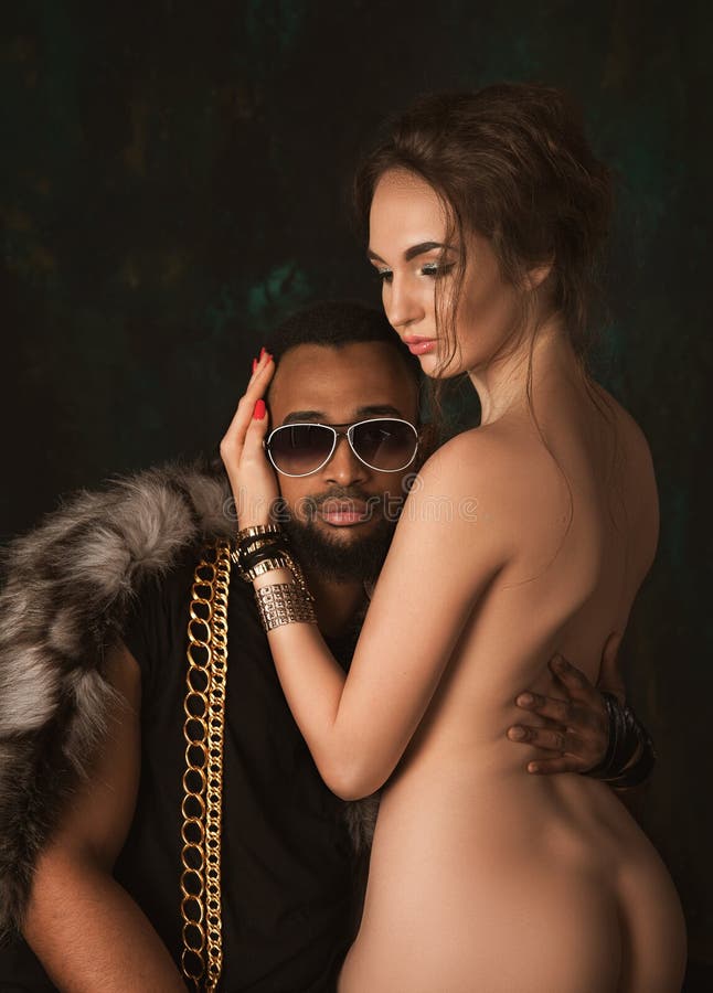 Black Man in Gold Chains and in an Expensive Fur Coat Hugging a White Naked Woman Stock Photo