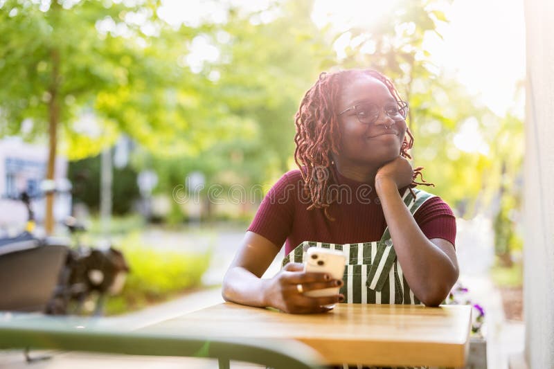 Black non-binary person sitting in an outdoor cafe stock photo