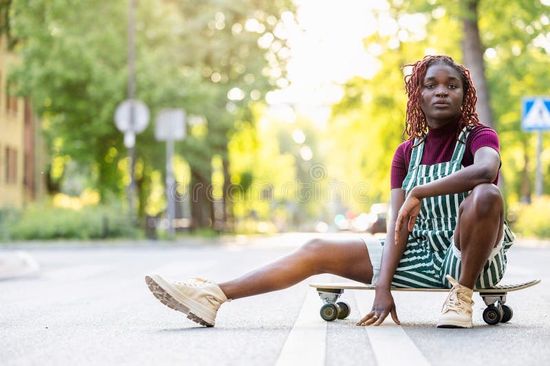 Black non-binary person with a skateboard sitting on the street stock photos