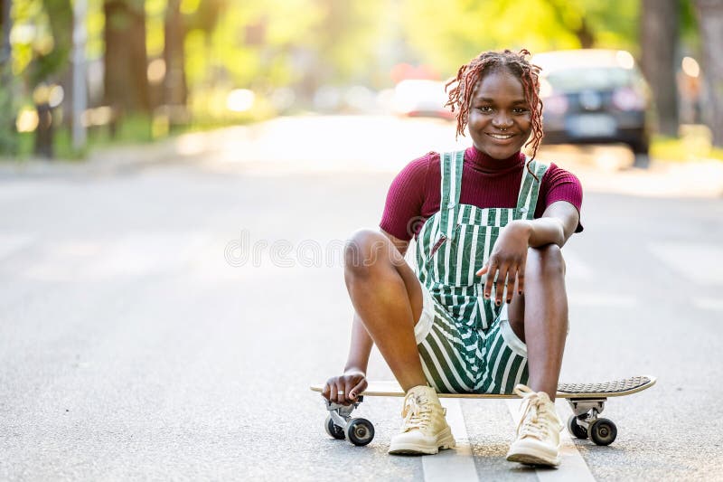 Black non-binary person with a skateboard sitting on the street stock photo