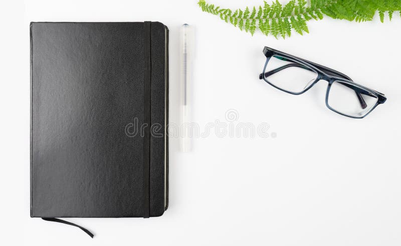 black notebook, pen and glasses on white table