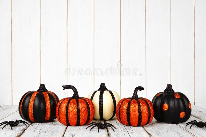 Black and orange glittery Halloween pumpkins against white wood