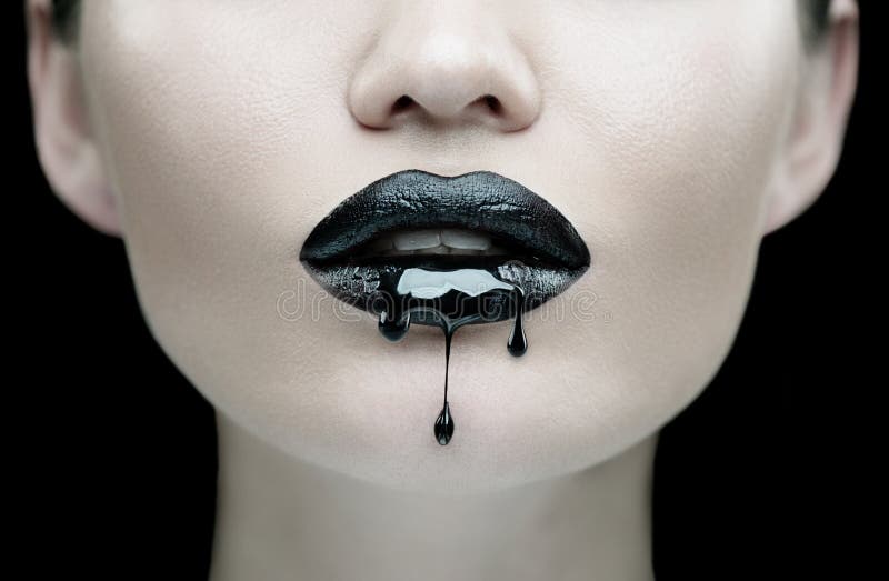 Black Paint dripping from the black lips, dark liquid drops on beautiful model girl`s mouth. Lipstick. Halloween party make-up