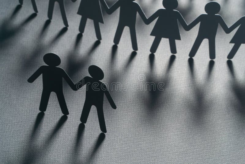 Black paper figure of a male couple in front of a crowd of paper people holding hands on white surface. Social movement