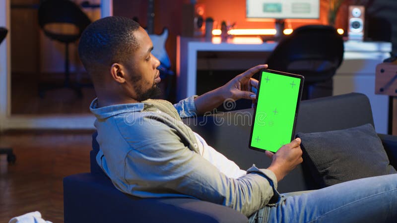 Black remote worker looking at green screen on his device at home stock photography
