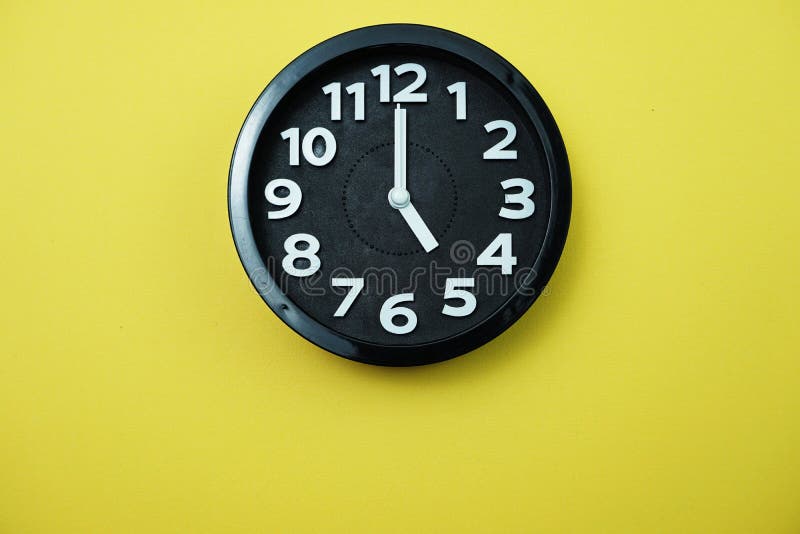 Black Round Clock Showing Five O`clock on Yellow Background Stock Image