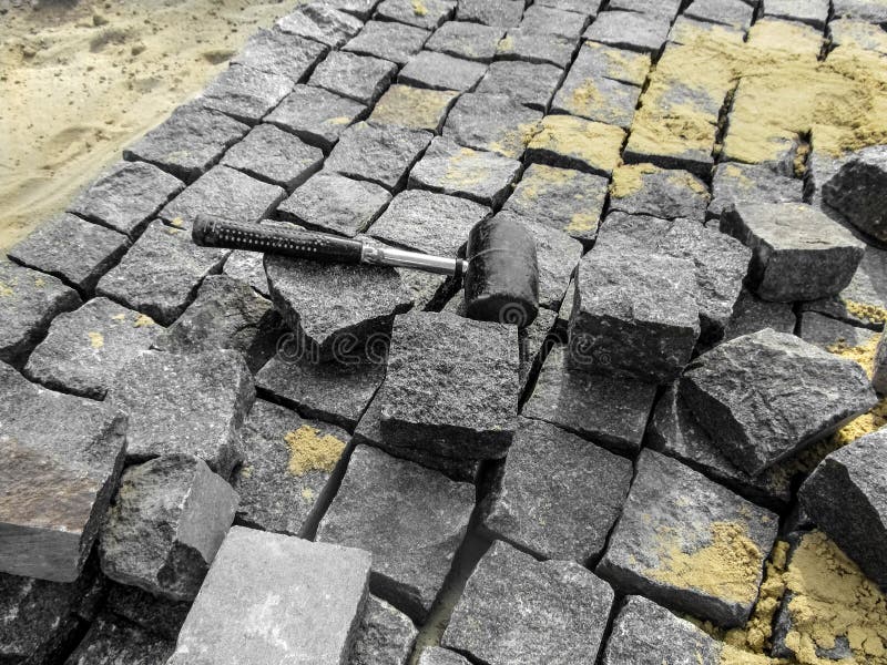 A black rubber mallet lies among gray granite stones on the surface of a new paving slabs. Beautiful building background royalty free stock photo