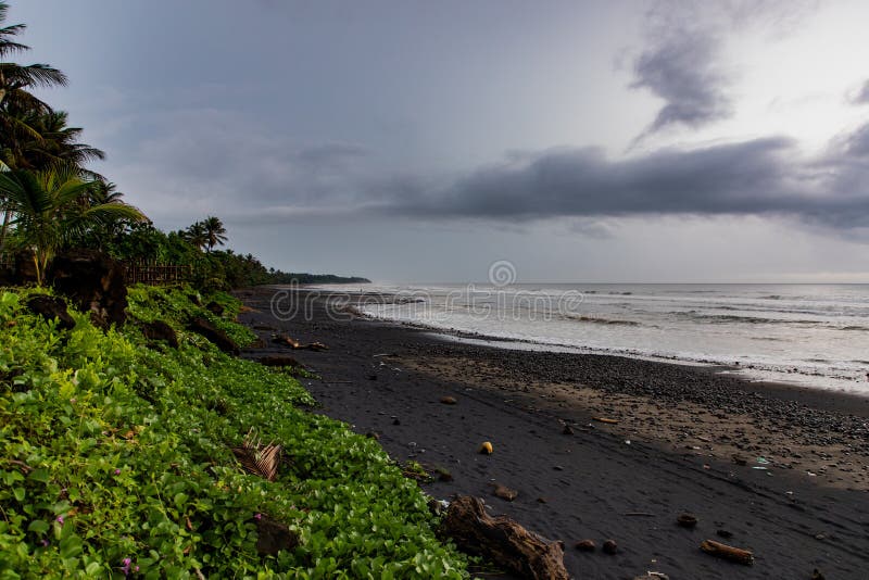 Black sand beach with green vegetation in a stormy day in Bali, Indonesia royalty free stock photo Black sand beach with green vegetation in a stormy day in Bali, Indonesia royalty free stock photo