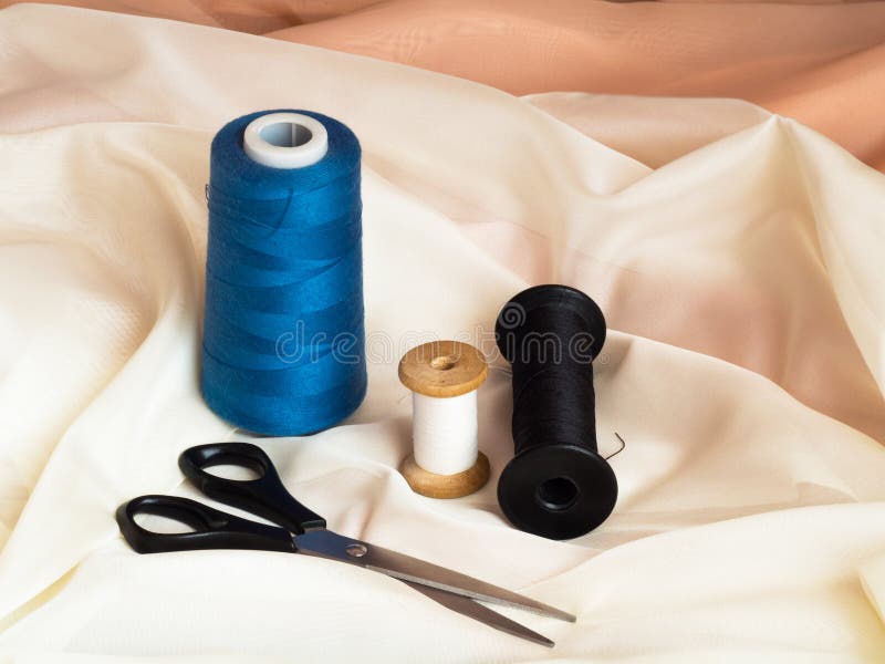 Black scissors and three threads of different colors on beige fabric, macro shot, sewing concept
