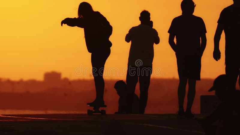 Black silhouettes of people on the hill at sunset - a woman riding skateboard