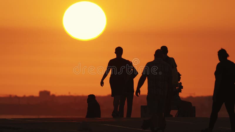 Black silhouettes of people spending time on the hill and walking out their pets at sunset