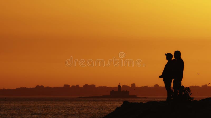 Black silhouettes of two men standing on the hill at sunset