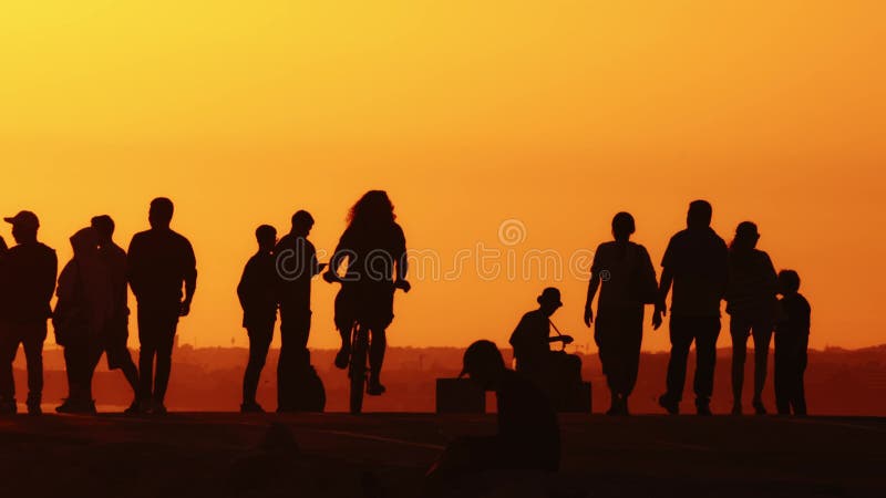 Black silhouettes of young and free people on the hill at sunset