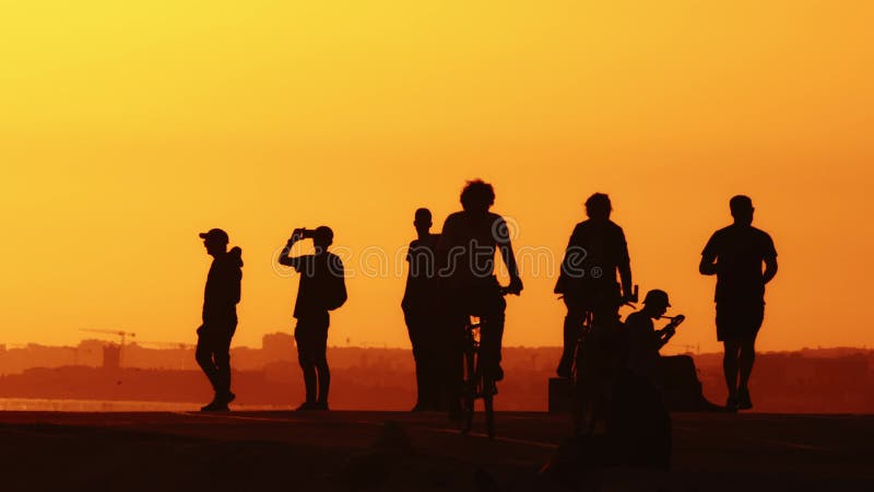 Black silhouettes of young people on the hill at sunset - people riding bikes