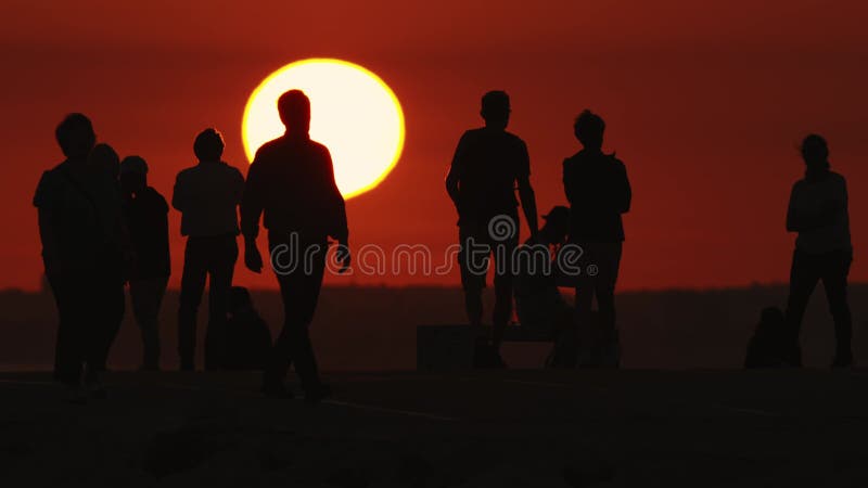 Black silhouettes of young people spending time on the hill at bright red sunset