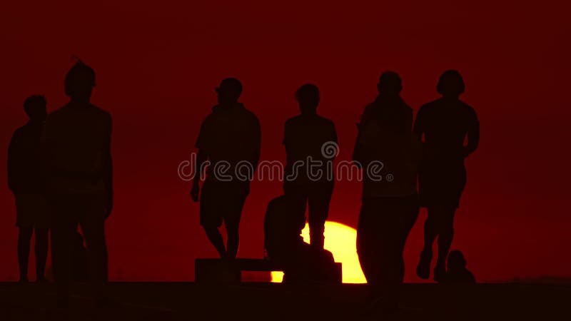 Black silhouettes of young people spending time on the hill at red sunset