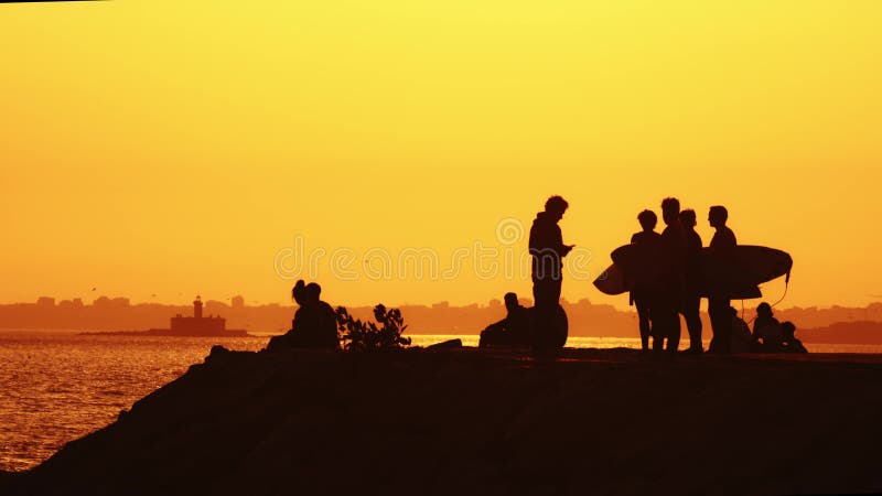 Black silhouettes of youth holding surfing boards at sunset