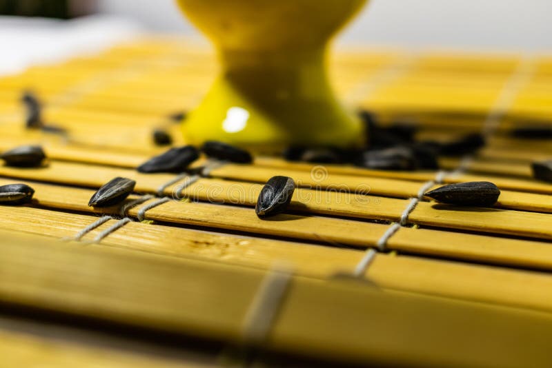 Black small sunflower seeds. Click seeds with husks. A handful in a yellow miniature stand on a wooden napkin. Spilled some seeds. Round small bowl with an openwork pattern.