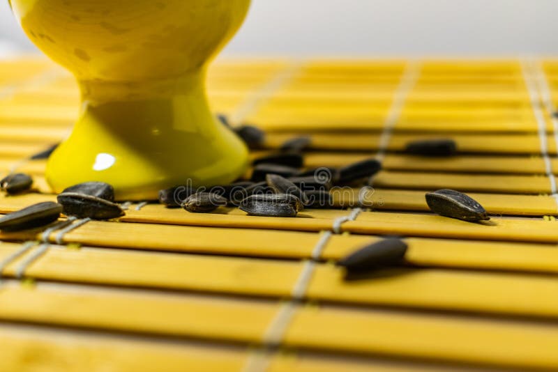 Black small sunflower seeds. Click seeds with husks. A handful in a yellow miniature stand on a wooden napkin. Spilled some seeds. Round small bowl with an openwork pattern.