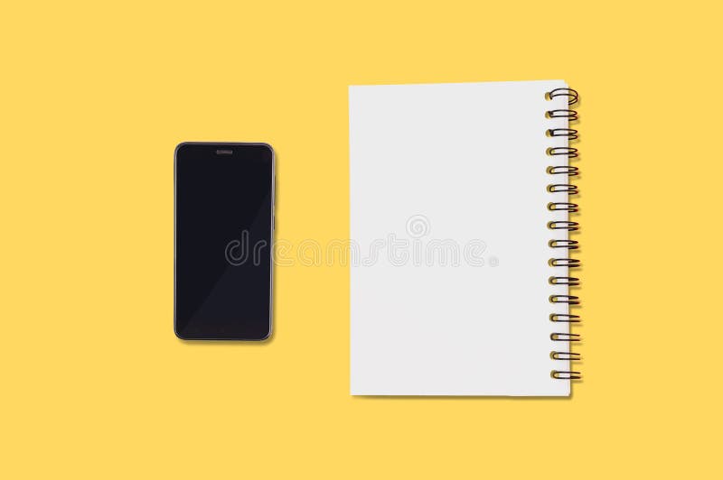 Black smartphone and blank paper notepad with spiral holder lies on yellow table in office or home. Top view