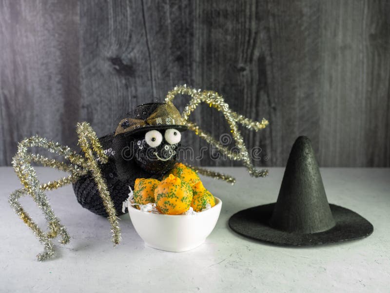 Black Spider with gold pipe cleaner legs Posing with a white bowl full of orange and green Carrot Cake Balls and a black witch hat