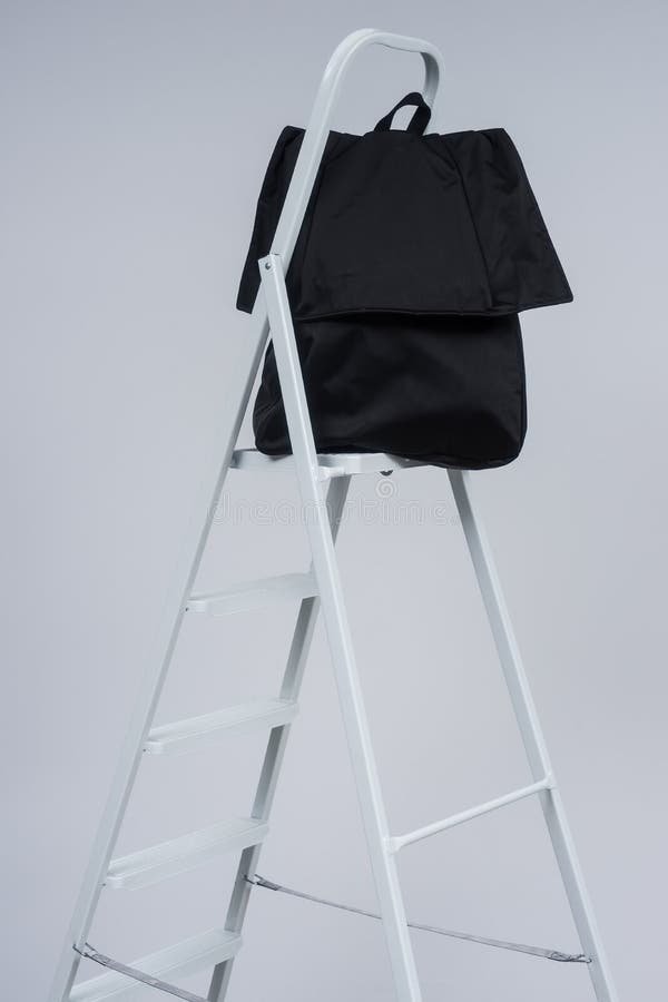 Black Stylish Casual Backpack on the Top of the White Ladder. Stock