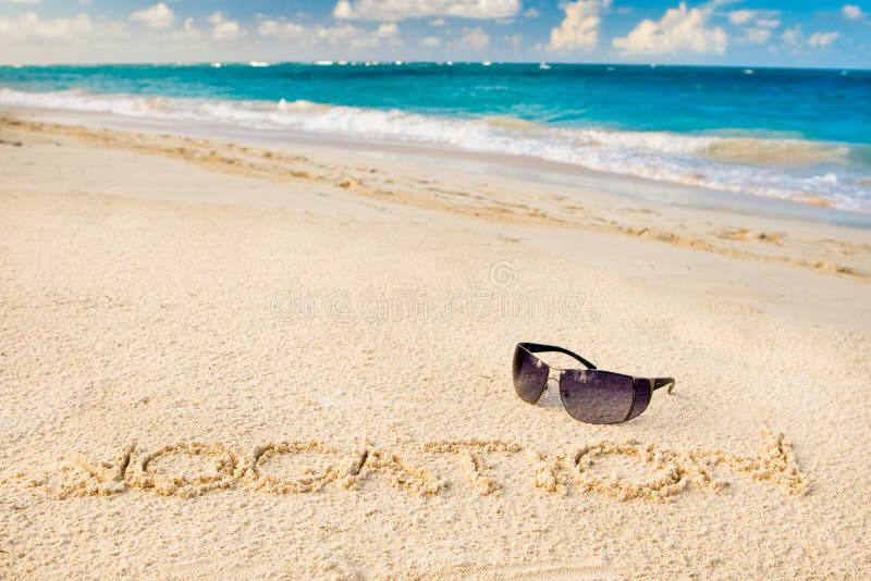 Black sun glasses on white sand beach