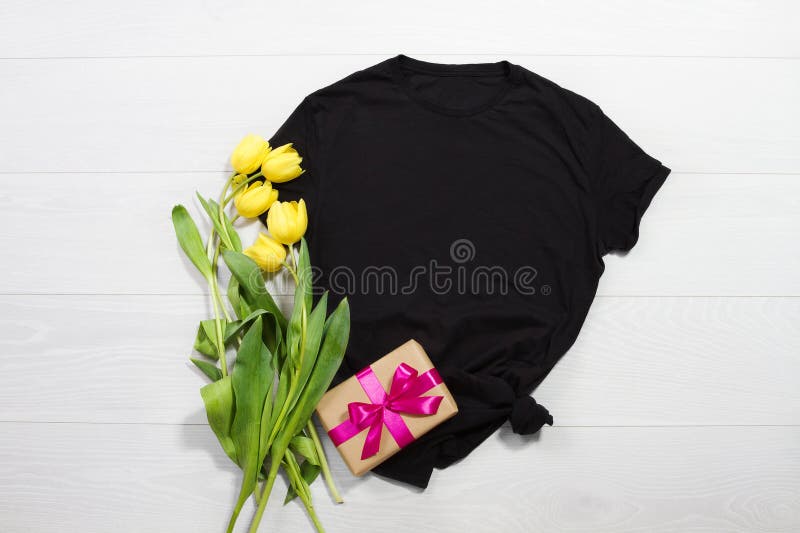 Black t-shirt mockup. Template blank shirt top view. White wooden background. Mother women day holiday. Yellow tulips. Woman