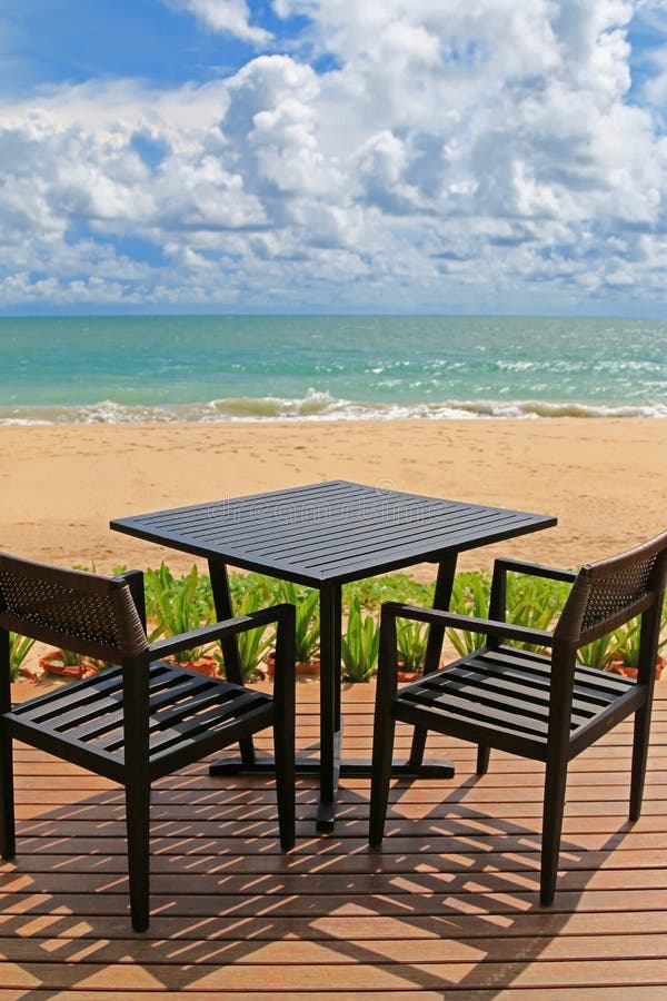 Black table for two on wooden balcony with blurred beach and blu