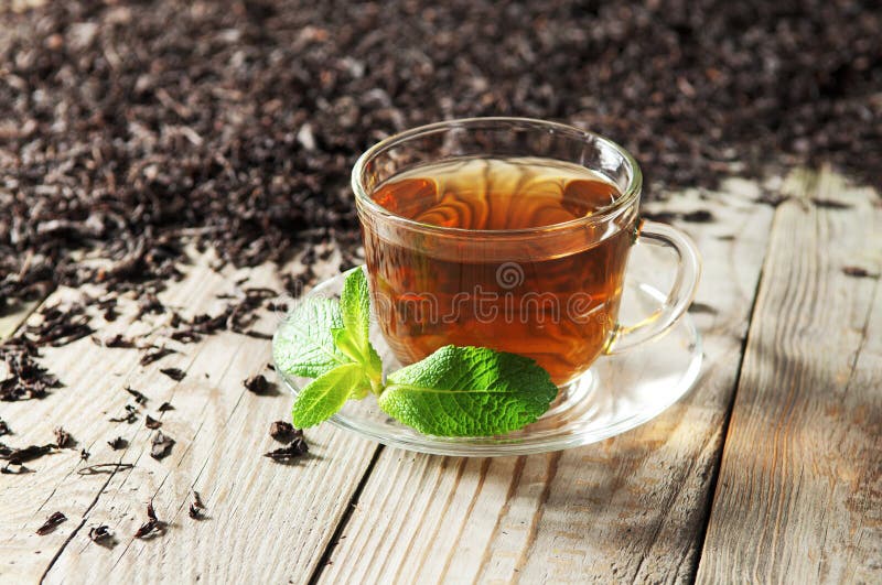 Black tea in a glass cup and saucer on a wooden table. Next to a cup of black tea scattered dry tea