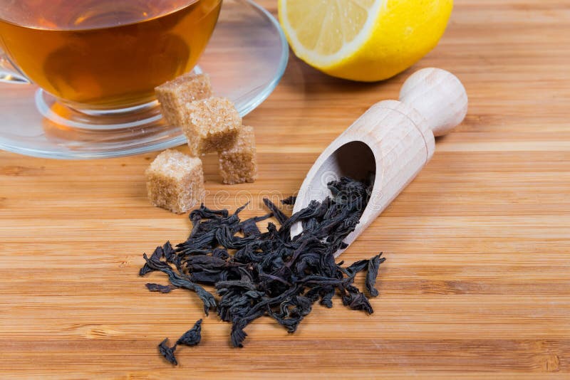 Black Tea Leaves, Tea Cup and Lemon on Wooden Surface Stock Image