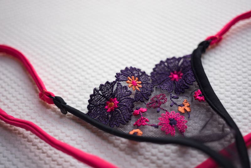 Black thongs made of transparent thin mesh with multi-colored embroidered flowers and pink elastic band on white fabric