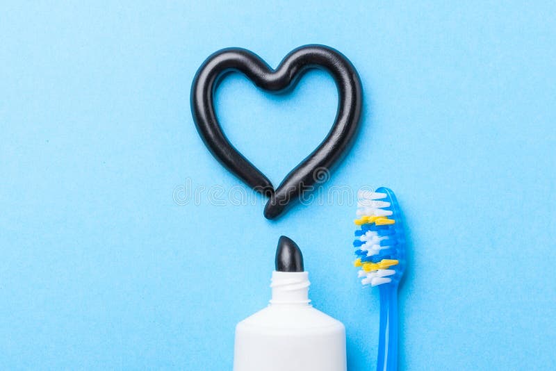 Black toothpaste from charcoal for white teeth. Tooth-paste in the form of heart, tube and toothbrush on blue