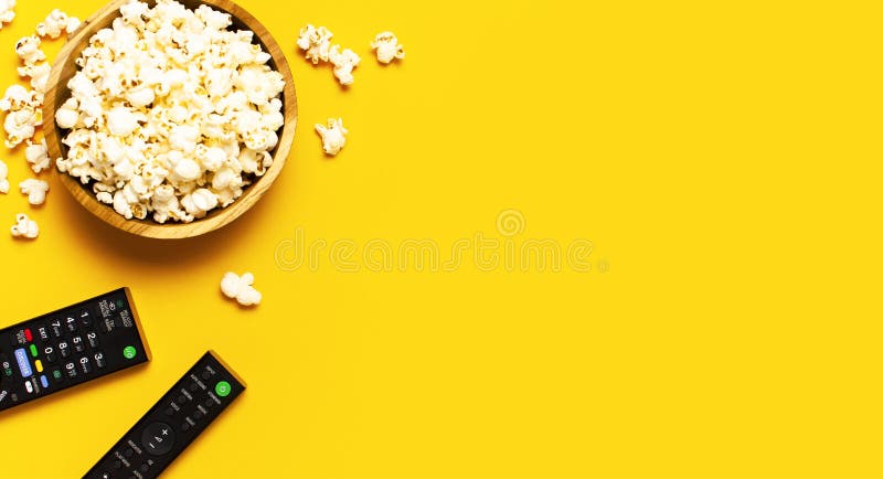 Black TV, audio remote control and popcorn on bright yellow background flat lay top view copy space. Minimalistic background with a remote control, watching a movie, series set-top boxes audio system