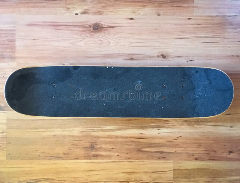 Black used skateboard on a light wooden background. royalty free stock photos