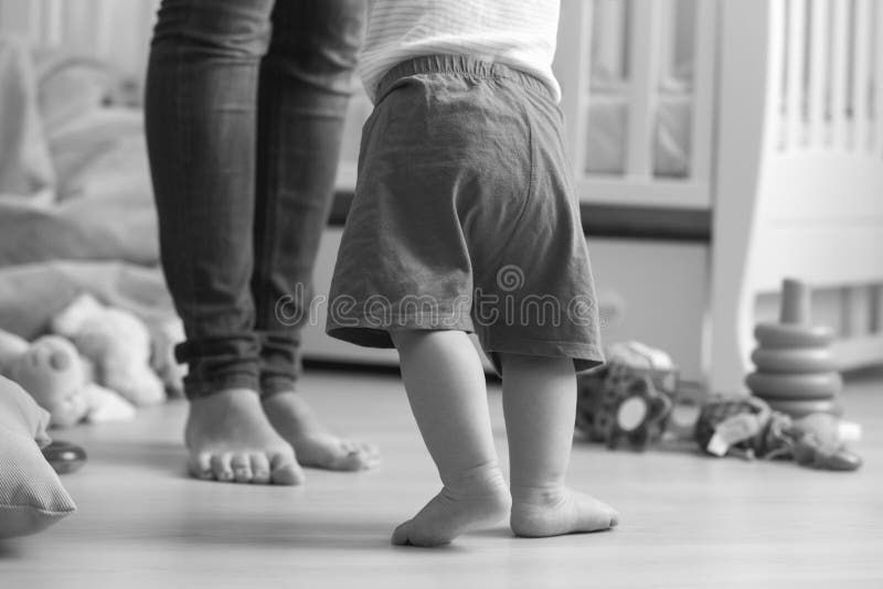Black and white image of 10 months old baby boy walking to his m