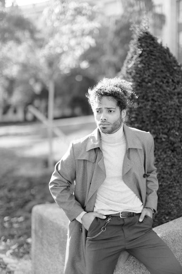 Black and white photo of afro american man standing in park near bush.