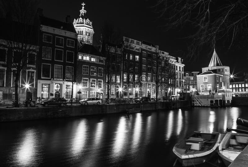 Black-white photo of cruise boat moving on night canals of Amsterdam in Amsterdam, Netherlands.