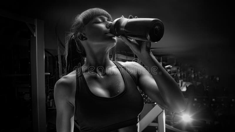 Black and white photo of fitness woman drinking water from bottle Muscular young female at gym taking a break from workout stock image Black and white photo of fitness woman drinking water from bottle Muscular young female at gym taking a break from workout stock image