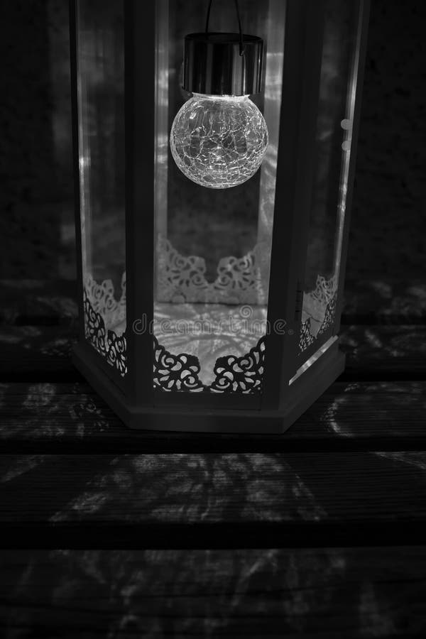 Black and white photo of an illuminated lantern throwing beautiful floral shadows on a wooden bench royalty free stock images