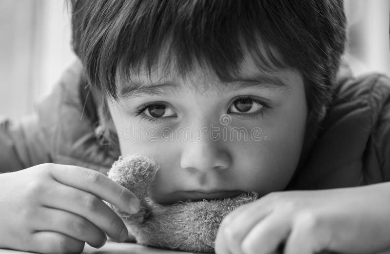 Black and white photo of Kid with bored face,Lonely boy putting his chin down on teddy bear and looking out, Upset preschool child